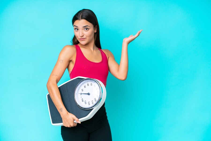 young-caucasian-woman-isolated-blue-background-with-weighing-machine